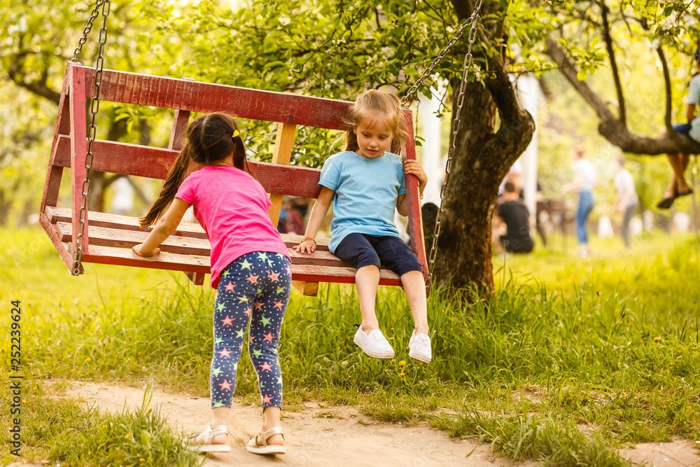Fototapeta premium Smiling little girl on a swing. Children playing outdoors in summer
