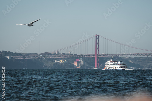Boat in the Tagus (Tejo) river. The 25 de Abril Bridge (Ponte 25 de Abril) in the background, a suspension bridge which connects the city of Lisbon to the municipality of Almada.