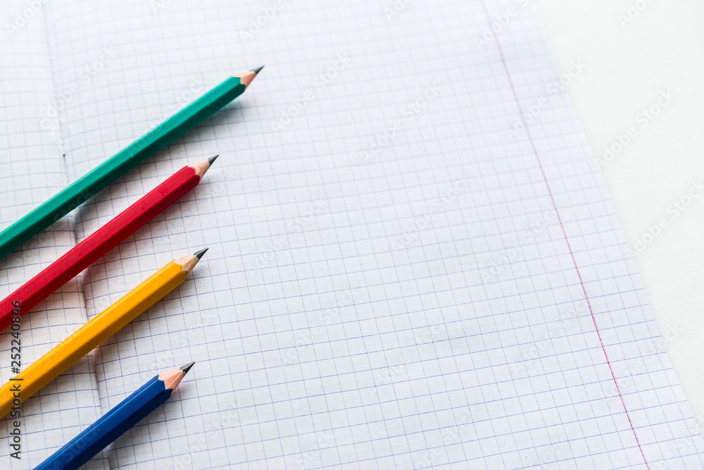 Multicolored pencils on a notebook in a cage Multicolored pencils on a notebook in a cage