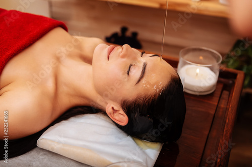 Good-looking naked woman peaceful resting while stream of oil covering