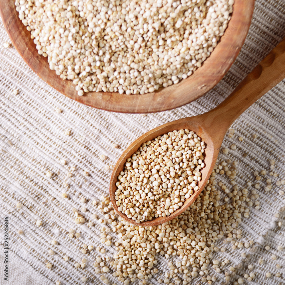 Raw organic superfood gluten free quinoa seeds in wooden spoon and bowl on kitchen table closeup Raw organic superfood gluten free quinoa seeds in wooden spoon and bowl on kitchen table closeup