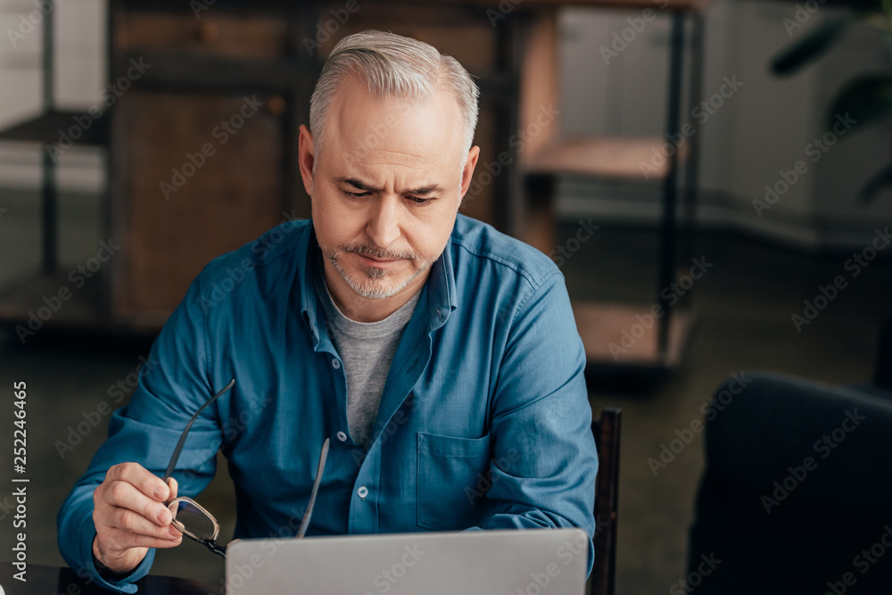 Fototapeta premium tired man looking at laptop while holding glasses