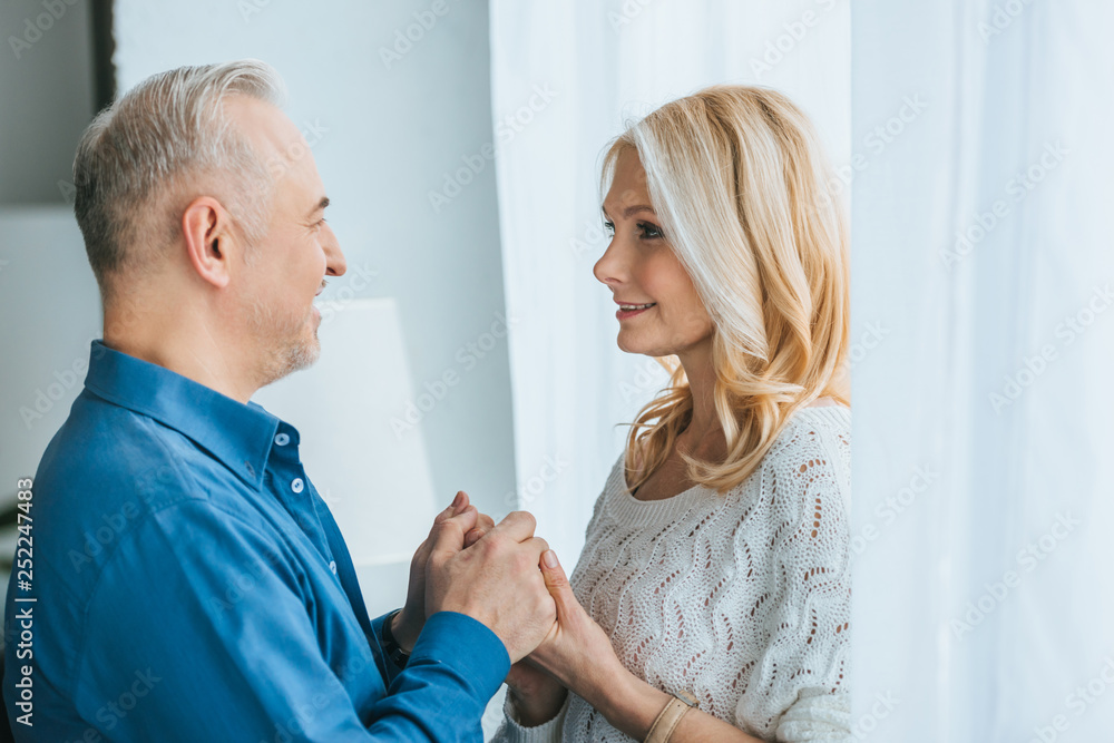 cheerful couple smiling while holding hands at home cheerful couple smiling while holding hands at home