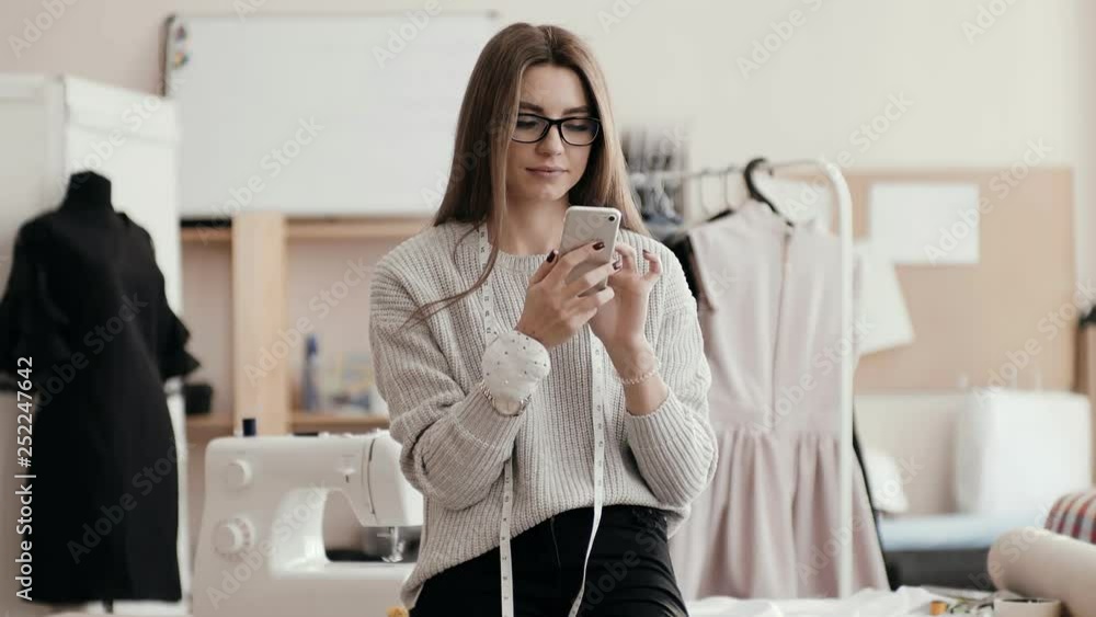 seamstress looks at the phone in a serious face, looks at the camera and smiles. seamstress looks at the phone in a serious face, looks at the camera and smiles.