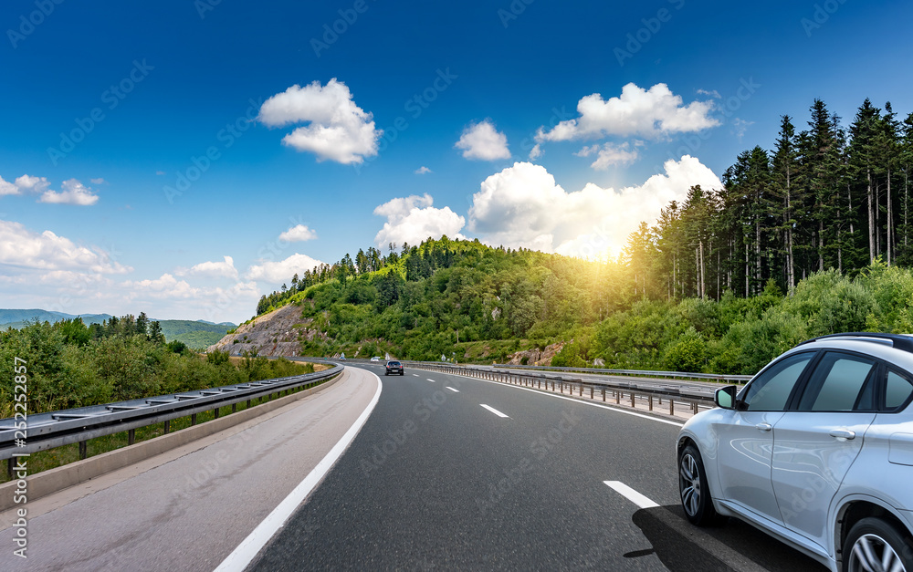 Car driving on highway surrounded by picturesque mountains.