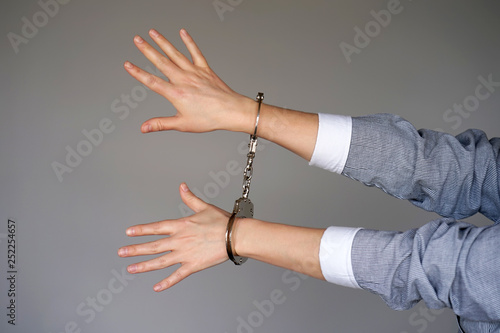 Arrested woman handcuffed hands. Prisoner or arrested terrorist, close-up of hands in handcuffs isolated on gray background. Criminal female hands locked in handcuffs.
