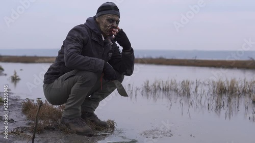 An angry mutamt monster with big machete coming to the river and taste a water in unkind cloudy weather. Horror Character concept, Armed and grasepainted entity photo