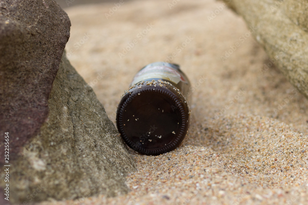 brown bottle laying on sand between to rocks brown bottle laying on sand between to rocks