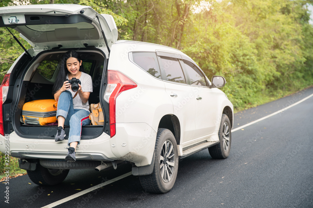Woman traveler and camera sitting on hatchback car with natural background . Young traveler woman taking a photo and sitting on hatchback car . Woman traveler and camera sitting on hatchback car with natural background . Young traveler woman taking a photo and sitting on hatchback car .