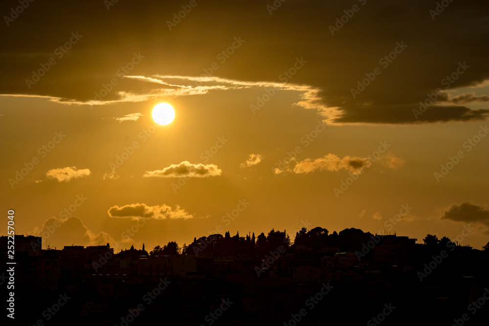 Amazing sky, Sun just below puffy clouds and town silhouette view of ancient town of Matera, the Sassi di Matera, Basilicata, Southern Italy, cloudy summer afternoon just before sunset