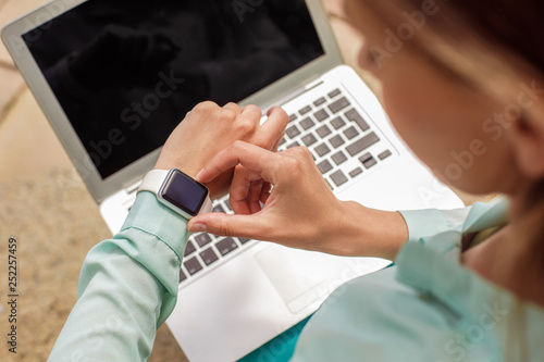 Young woman sitting on stairs working on laptop checking time on watch close-up top view