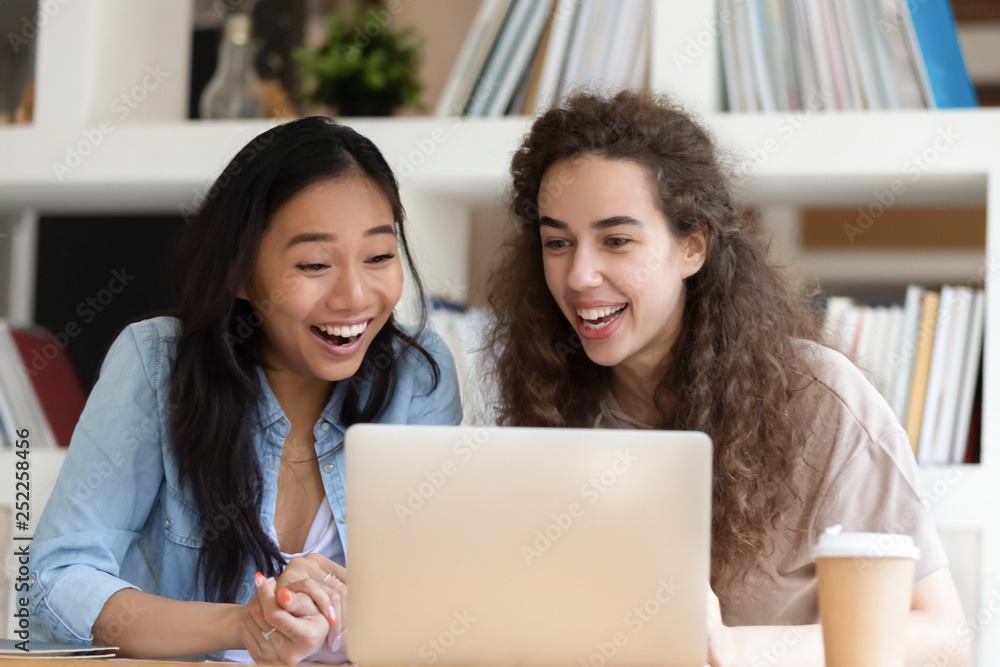 Happy cheerful asian and caucasian girls laughing looking at laptop Happy cheerful asian and caucasian girls laughing looking at laptop