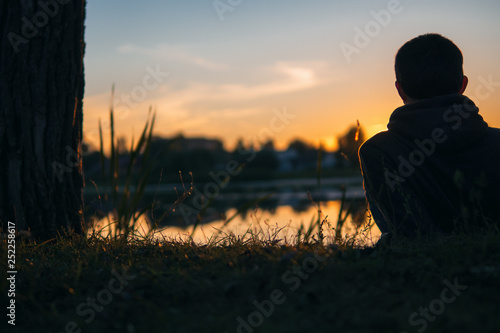 Dreaming man on the lake against the background of a beautiful evening sunset