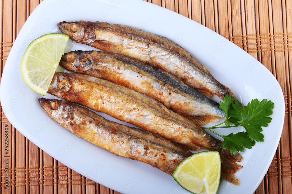 Deep frying small fish capelin and sliced lemon on white plate. Good snack to beer. Deep frying small fish capelin and sliced lemon on white plate. Good snack to beer.
