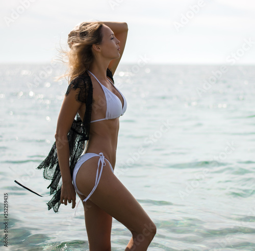 Young beautiful blond fashion woman wearing white swimsuit and black lace beach cape stay in the sea