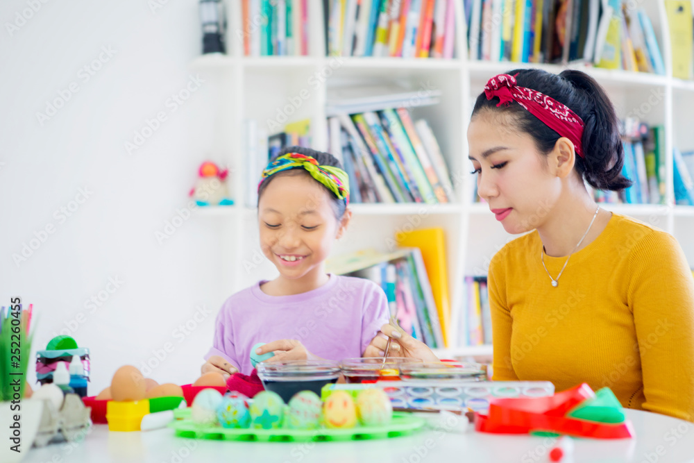 Naklejka premium Happy little girl paints eggs with her mother