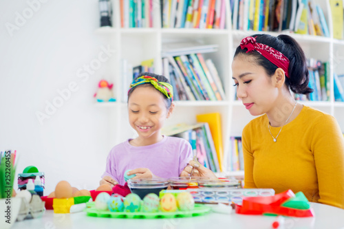 Happy little girl paints eggs with her mother