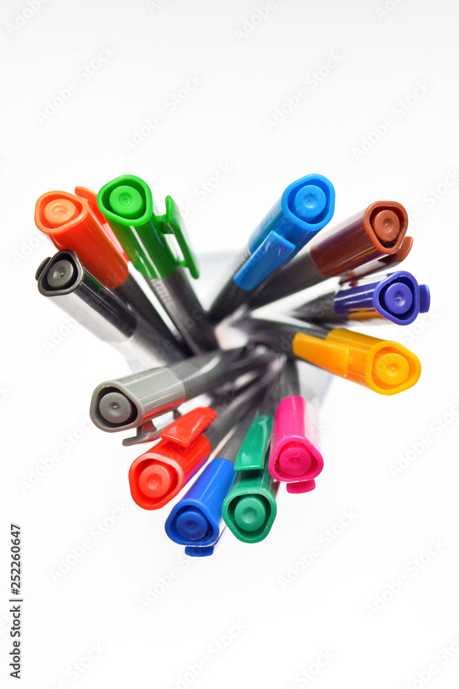 Set of multi-colored pens standing in a transparent glass, top view on white background, isolated, vertically oriented Set of multi-colored pens standing in a transparent glass, top view on white background, isolated, vertically oriented
