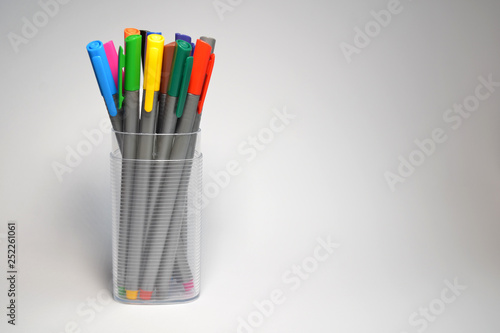 Set of multi-colored pens standing in a transparent glass, side view on white background with shadow with copyspace