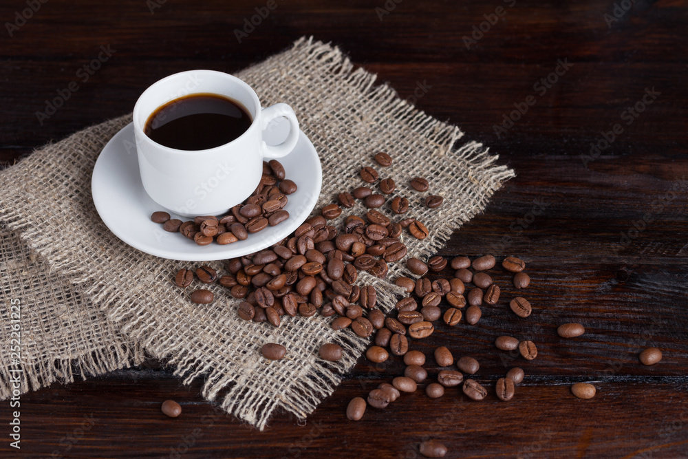 White cup of coffee with coffee grains near on linen fabric on the dark vintage background