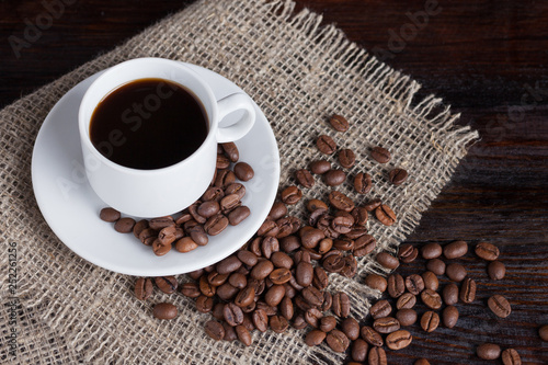 White cup of coffee with coffee grains near on linen fabric on the dark vintage background