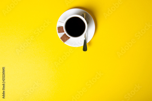 Cup of coffee with chocolate pieces on yellow background, top view