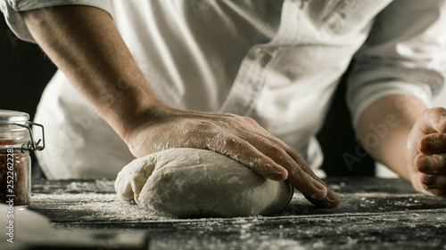 Male chef hands knead dough with flour on kitchen table photo