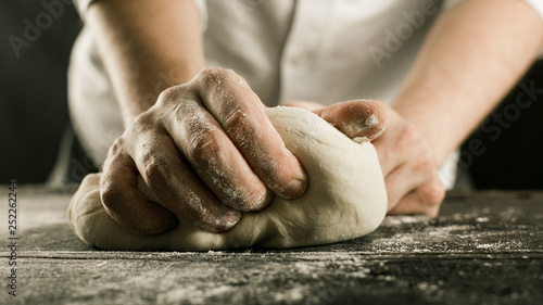 Male chef hands knead dough with flour on kitchen table