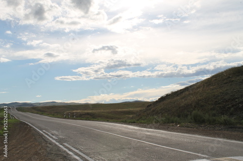 road in steppe under a blue sky with white clouds Sayan mountains Siberia Russia © lkurganskaya