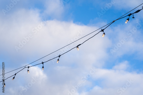 Lightbulbs strung with wire, illuminated, against a blue sky with clouds