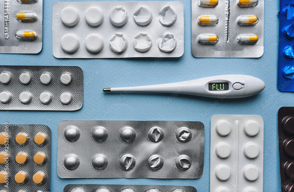 Electronic thermometer from the scoreboard on which it is written - FLU. Pills in blister packs on blue background. The concept of a cold and its treatment. Traditional medicine. Electronic thermometer from the scoreboard on which it is written - FLU. Pills in blister packs on blue background. The concept of a cold and its treatment. Traditional medicine.