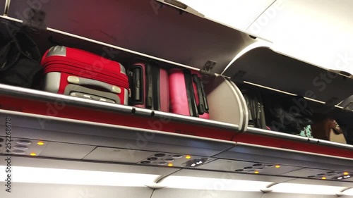 Close-up of bright suitcases lying on the shelves in the plane. Economy class cabin of typical airliner.