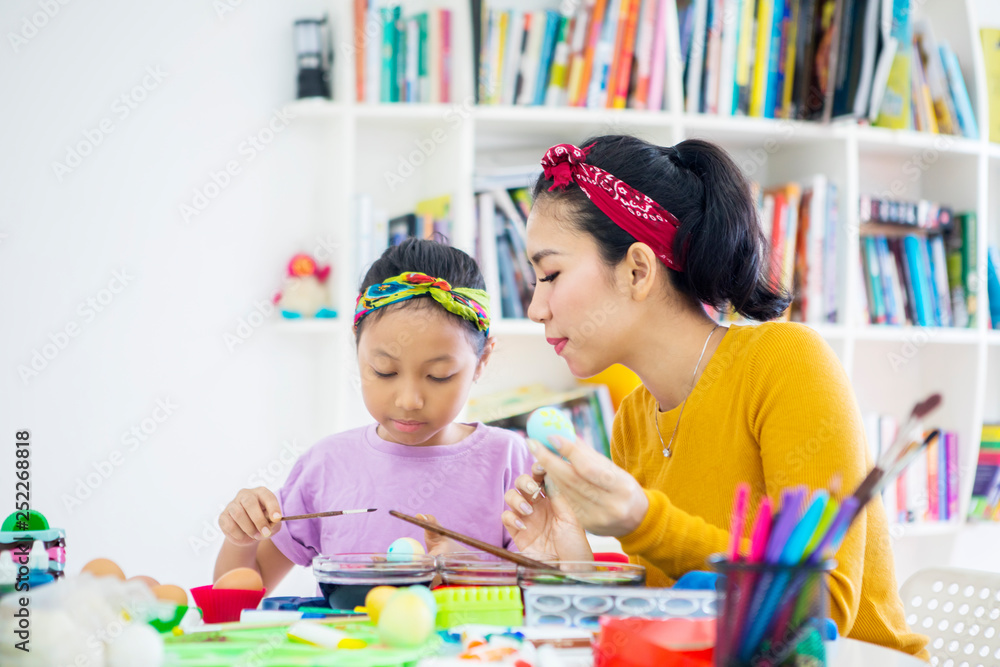 Fototapeta premium Young woman and her daughter colors Easter eggs