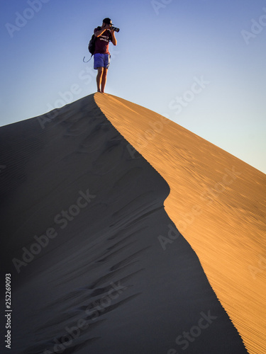 man on top of sand dune taking photos photo