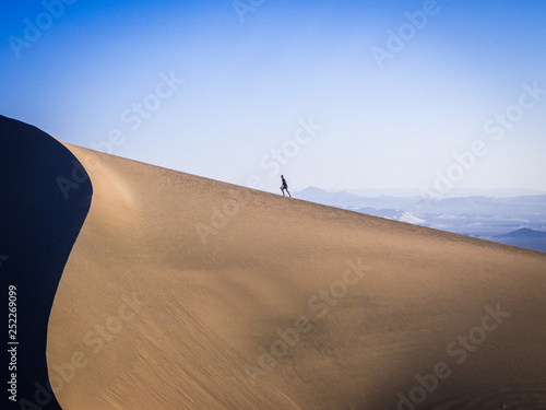 man walking up sand dunes in the desert photo