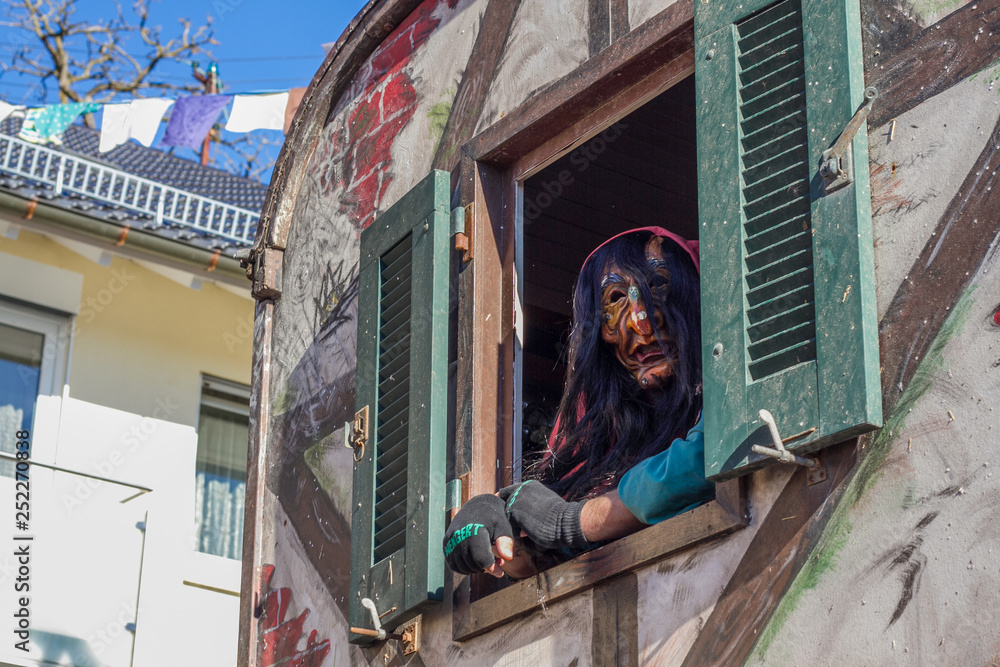 Hexe schaut aus Fenster - Traditionelle Kostüme der schwäbisch-alemannischen Fasnet mit Holzmasken bei einem Festumzug in Ammerbuch, Baden-Württemberg