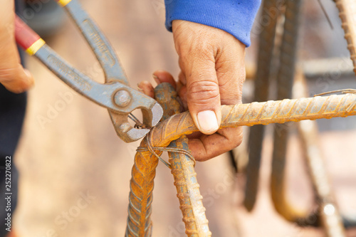 Close up image of construction worker securing steel bars with wire rod for reinforcement of cement work at construction site