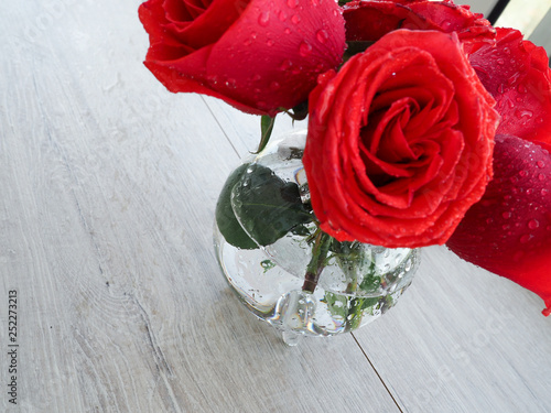 Preparing a gift, on a wooden table, with roses. Female hand holding a gift, wrapped with ribbon, on a background of red roses, the space under the text. photo