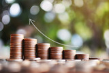 Coins arranged vertically with graph pointing up on wood plank and tree bokeh background , Saving and growing business concept, selective and soft focus.