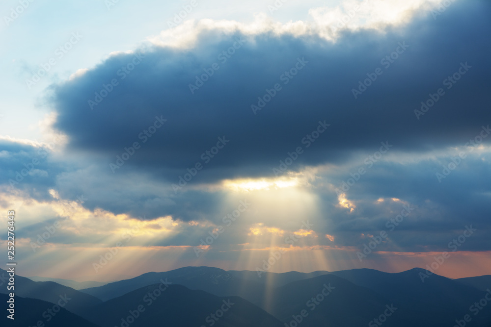 Dramatic sunset in the spring Ukrainian carpathians with red skies, rays and dark clouds, against the background of mountain ridges covered with alpine pine.