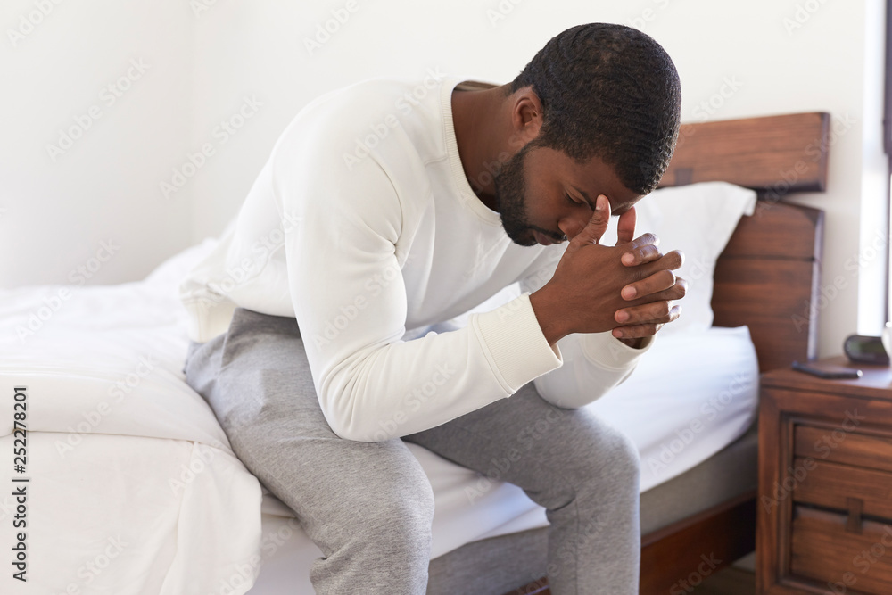 Depressed Man Looking Unhappy Sitting On Side Of Bed At Home With Head In Hands Depressed Man Looking Unhappy Sitting On Side Of Bed At Home With Head In Hands