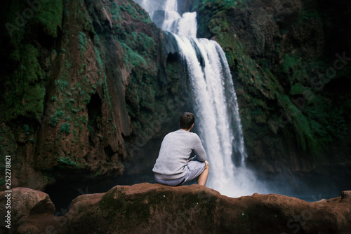 Young man sitting on a stone against Ouzoud waterfalls - Morocco, Africa. Concept of travel.  photo