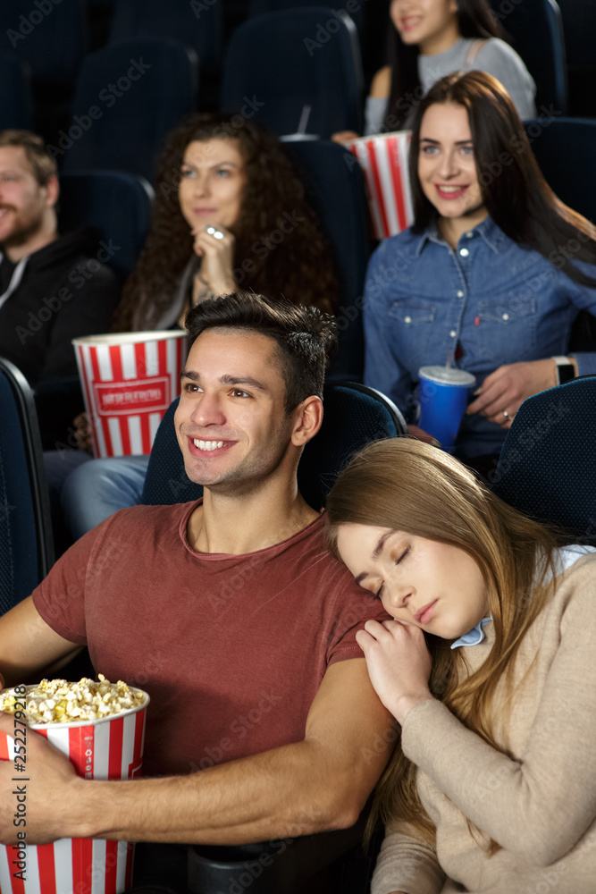 Beautiful young woman sleeping on her boyfriend’s shoulder during the movie