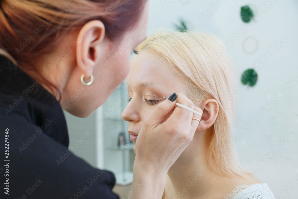 Process of making makeup. Make-up artist working with brush on model face. Portrait of young blonde woman in beauty saloon interior. Applying tone to skin. Process of making makeup. Make-up artist working with brush on model face. Portrait of young blonde woman in beauty saloon interior. Applying tone to skin.