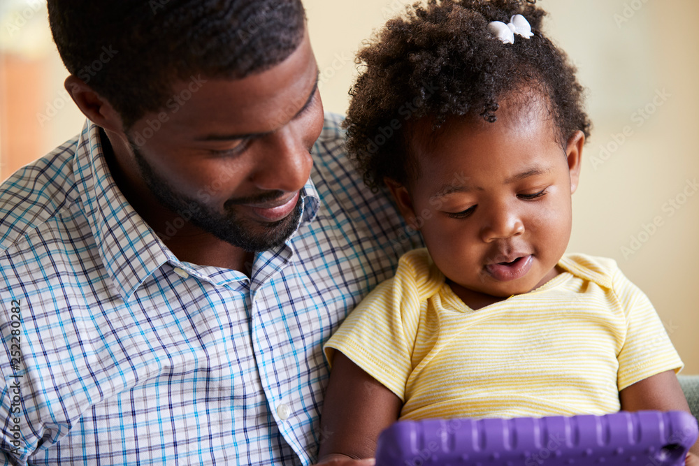 Baby Daughter And Father Playing With Toy On Sofa In Lounge At Home
