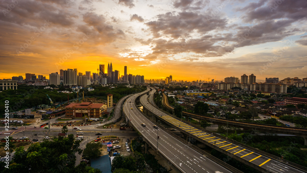 Kuala Lumpur city skyline during dramatic sunset with elevated highway leading into the city.