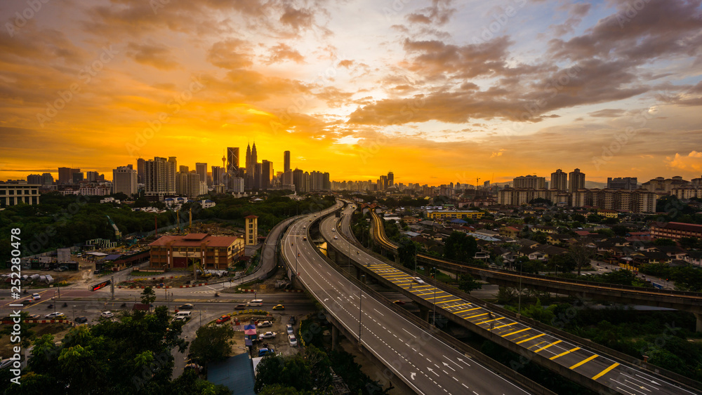 Kuala Lumpur city skyline during dramatic sunset with elevated highway leading into the city.