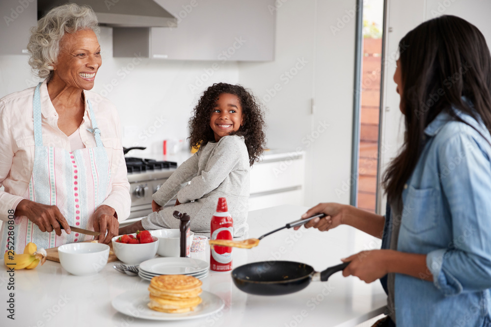 Multi Generation Female Family In Kitchen At Home Making Pancakes Together