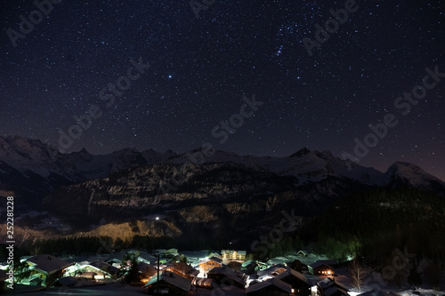 Winter mountain village in Hasliberg Hohfluh illuminated in a dark clear cold night with a sea of ​​stars and mountain range covered with snow in Switzerland, Europe. photo