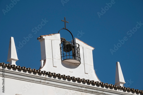 Bell and cross on the roof of a small white chapel in Marbella, Spain.